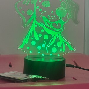May include: A green LED night light shaped like a Dalmatian dog with black spots. The light is on a black base and has a cord.