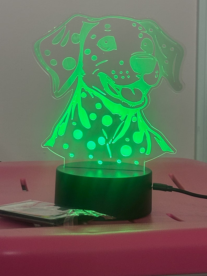 May include: A green LED night light shaped like a Dalmatian dog with black spots. The light is on a black base and has a cord.