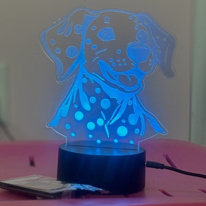 May include: A blue night light shaped like a Dalmatian dog with black spots. The light is on and illuminating the dog's face.
