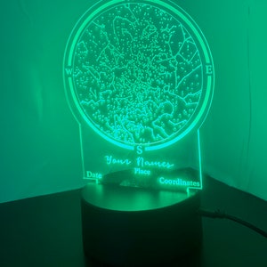 Op de afbeelding: Een groen nachtlampje met een cirkelvormig ontwerp dat een sterrenkaart voorstelt. Het lampje heeft een zwarte voet en bevat de tekst "Your Names", "Date", "Place" en "Coordinates".