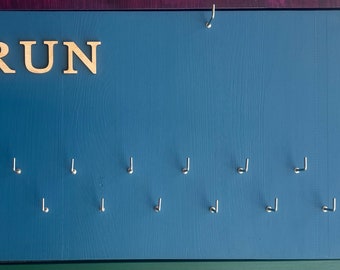 May include: A blue wooden board with the word "RUN" in gold letters. The board has 12 hooks for hanging medals or other items.