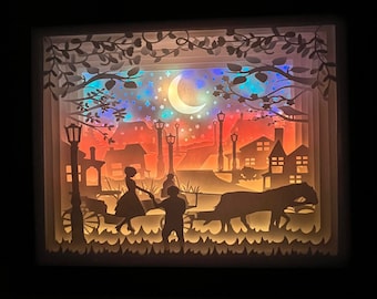 Könnte beinhalten: Ein Papier-Schnittbild, das ein Paar zeigt, das Hand in Hand unter einem Halbmond geht. Die Szene spielt in einer Stadt mit Straßenlaternen und Gebäuden. Das Paar ist vor einem bunten Hintergrund silhouettiert.