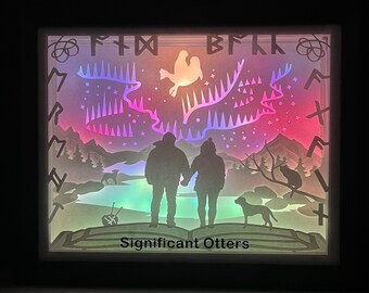 Puede incluir: Una caja de luz con un diseño de aurora boreal colorido, dos figuras de pie frente a un bosque, un perro y el texto "Significant Otters".