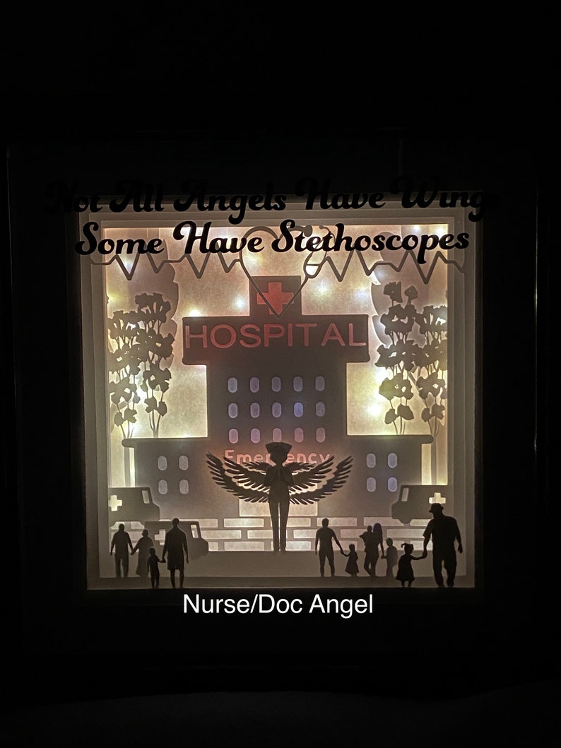 May include: A papercraft shadow box with a silhouette of an angel with wings, a hospital building, and a family. The text "Not All Angels Have Wings Some Have Stethoscopes" is at the top of the box. The text "HOSPITAL" is on the building. The text "Nurse/Doc Angel" is at the bottom of the box.