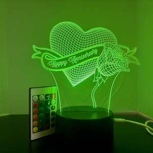 以下が含まれることがあります： ハート、バラ、バナーのデザインが施された緑色のLEDナイトライト。バナーには「Happy Anniversary」と書いてあります。ライトにはリモコンが付いています。