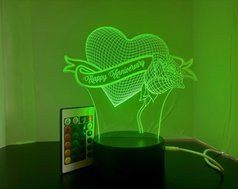 Puede incluir: Luz nocturna LED verde con un diseño de corazón, rosa y pancarta. La pancarta dice "Happy Anniversary". La luz viene con un control remoto.