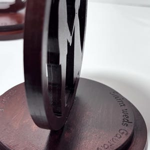 K&ouml;nnte beinhalten: Dunkelbraune Hochzeitsdekoration aus Holz mit einer Silhouette eines Paares, das sich an den H&auml;nden h&auml;lt, in einem kreisf&ouml;rmigen Rahmen. Die Basis ist rund, mit der Aufschrift "Saira weds Gaurav."