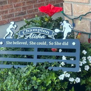 May include: Black metal plaque with a white silhouette of a tennis player, the text "Champion Alisha" and the quote "She believed, She could, So She did".