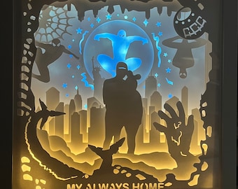 Puede incluir: Una caja de luz cuadrada con recortes de papel en capas que muestran el horizonte de una ciudad, figuras de Spider-Man y la Estatua de la Libertad. La escena está iluminada con luz azul y amarilla, con el texto MY ALWAYS HOME abajo.