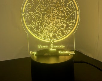 Puede incluir: Una luz nocturna personalizada con un mapa de estrellas, sobre una base negra y un panel de acrílico transparente. El panel muestra un mapa de constelaciones con las palabras "Tus Nombres", "Fecha", "Lugar" y "Coordenadas" impresas debajo del mapa.