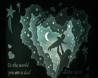 Puede incluir: Una silueta negra de un padre sosteniendo a un niño en el aire sobre un fondo de una nube en forma de corazón con estrellas y una luna creciente. El texto "To the world you are a dad. To me you are the world" está en el lado izquierdo de la imagen y "Love you DAD" está en el lado derecho.