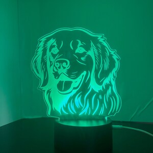 May include: A green LED night light shaped like a golden retriever dog's head. The light is on and illuminates the dog's face.