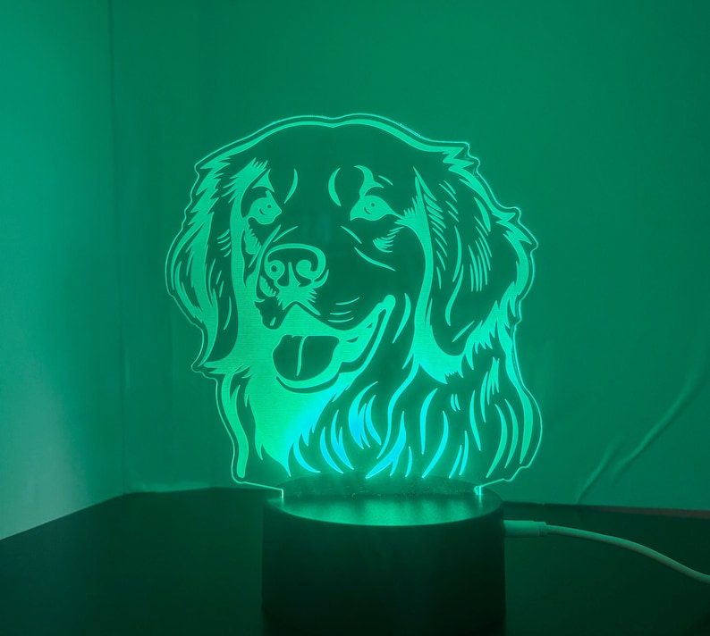 May include: A green LED night light shaped like a golden retriever dog's head. The light is on and illuminates the dog's face.