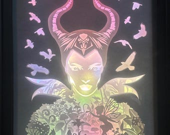 Puede incluir: Una obra de arte de papel recortado que representa a Maléfica de la película de Disney "La Bella Durmiente". La obra de arte presenta a Maléfica con sus cuernos y un hada en un entorno de bosque. La obra de arte está iluminada con un arcoíris de colores.