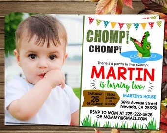 May include: A green alligator with a toothy grin is featured on a birthday invitation for a boy named Martin turning two. The invitation has a green, brown, and blue color scheme with a festive banner and a photo of the birthday boy. The text reads "There's a party in the swamp! Martin is turning two!" with details about the party date, time, and location.