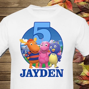 May include: White t-shirt with a blue circle featuring the characters from the children's show "The Backyardigans". The circle also includes the number "5" and the name "JAYDEN" in blue letters.