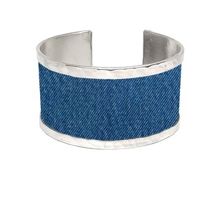 Op de afbeelding: Een zilveren armband met een denim inzet. De armband heeft een gehamerde metalen afwerking.