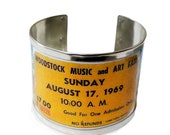 Entry ticket to the 1969 Woodstock Festival on a 4.5 cm wide bracelet. Made with recycled cans. Personalized internal text.