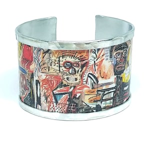 Op de afbeelding: Een zilveren metalen armband met een kleurrijke abstracte kunstprint met een menselijk gezicht en geometrische vormen.