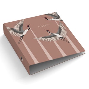 Peut inclure: Un classeur à trois anneaux avec une couverture rose clair. La couverture présente un motif de grues en vol aux ailes déployées, dans des tons de gris, de blanc et de rouge. Le mot "NOTES" est imprimé sur la couverture.