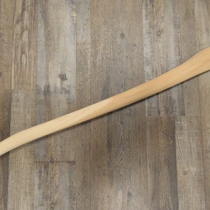 May include: A wooden axe handle with a natural finish. The handle is smooth and has a slight curve.