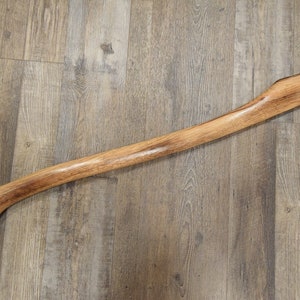 May include: A wooden axe handle with a natural finish. The handle is smooth and has a slight curve. It is approximately 36 inches long.