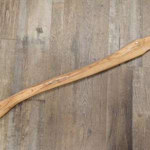 May include: A wooden axe handle with a natural finish. The handle is long and slender with a slight curve at the top.