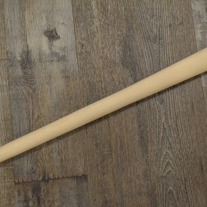 May include: A plain wooden handle for a hammer or other tool. The handle is light brown and has a smooth, rounded surface.