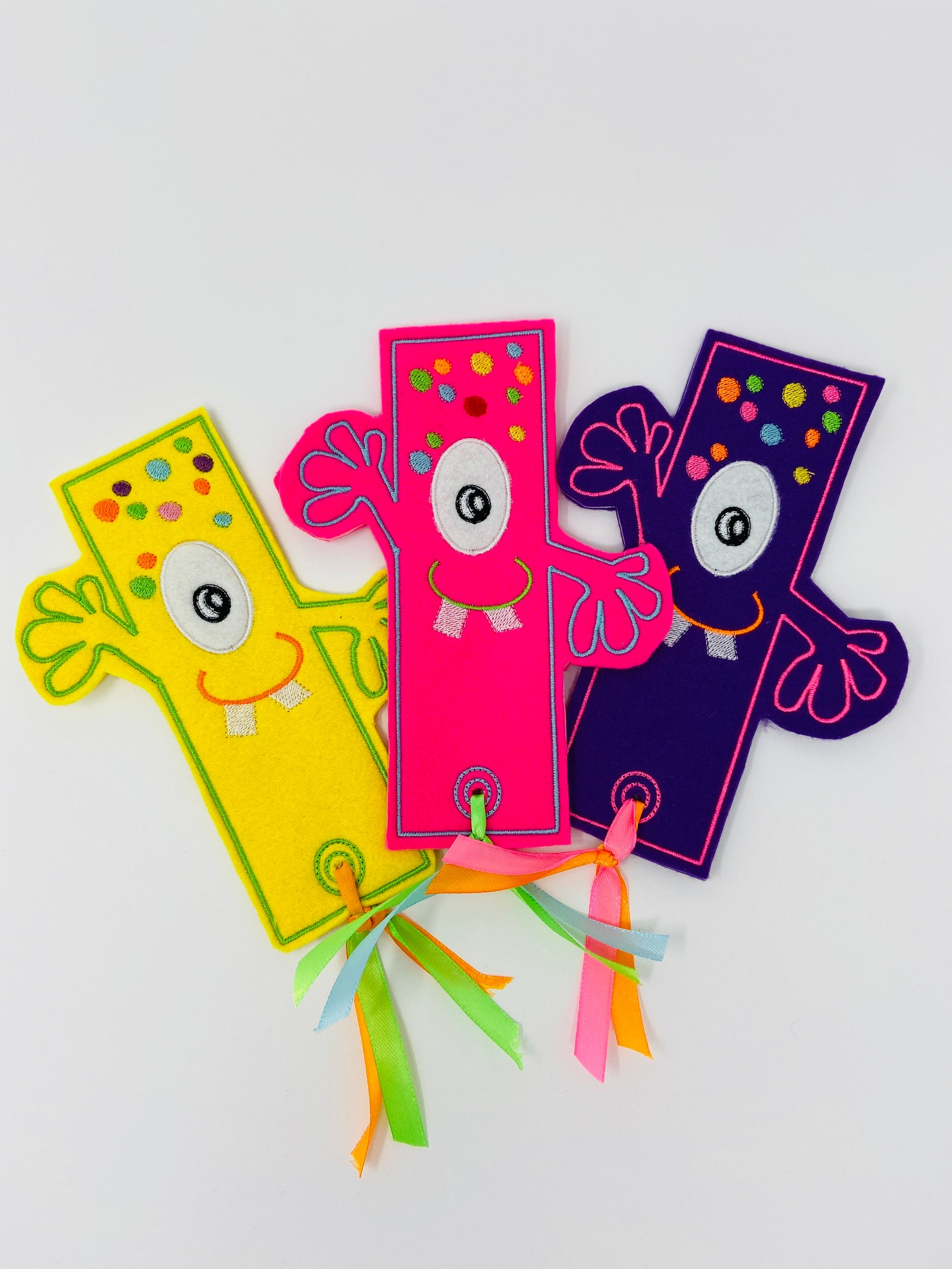 3 colourful embroidered monster bookmarks against a white background