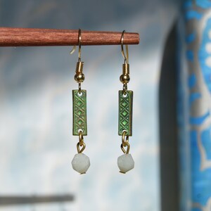 Peut inclure: Une paire de boucles d'oreilles pendantes dorées avec des breloques rectangulaires vertes et des accents de pierre blanche.