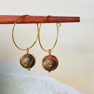 May include: Gold hoop earrings with a round, brown and red stone pendant.