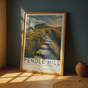 May include: A framed art print featuring a stylized illustration of Pendle Hill with a stone path leading up the grassy slope under a sunlit sky. The text reads PENDLE HILL followed by a description of the landmark and the 1612 witch trials.