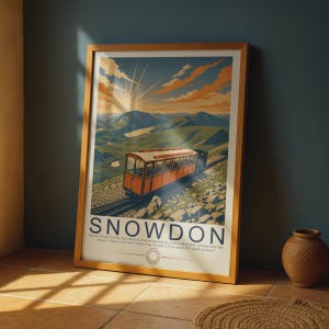 May include: A framed travel poster featuring an orange mountain railway train ascending a rocky slope toward a sunlit peak. The text reads SNOWDON, Mountain Railway Is The Only Public Rack-And-Pinion Mountain Railway In The United Kingdom.