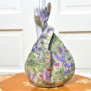 May include: A green and white floral print tote bag with a knotted handle. The bag features a variety of flowers, including daisies and lavender.