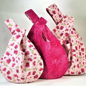 May include: Three pink fabric bags with a heart pattern. The bags are made of a soft, lightweight fabric and have a knotted handle.