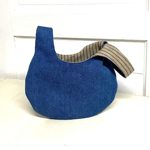 May include: A blue denim tote bag with a striped fabric lining. The bag has a single strap and a rounded shape.