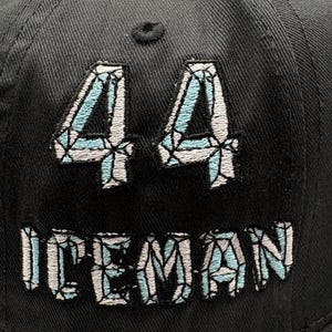 May include: Black baseball cap with the number "44" and the word "ICEMAN" embroidered in a light blue and white diamond pattern. The cap is made of a textured fabric.