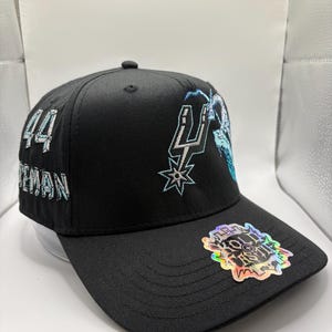 May include: Black baseball cap with embroidered team logo and the number "44" on the side. The cap features a holographic sticker on the brim. The team logo is in silver and light blue.