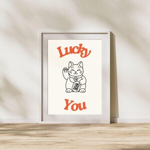 Könnte beinhalten: Ein weißer gerahmter Druck mit einer Schwarzweißillustration einer Glückskatze mit dem Text "Lucky You" in Orange.