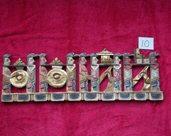 May include: A wooden wall hanging with a procession of carved figures in colorful clothing. The figures are holding musical instruments and carrying a palanquin. The piece is painted with gold accents and has a number "10" on a white tag.