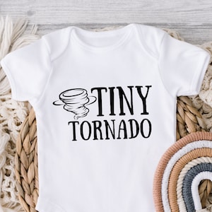 May include: White baby onesie with a black graphic of a tornado and the text "Tiny Tornado".
