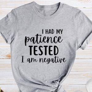 May include: Gray t-shirt with black text that reads "I had my patience tested I am negative".
