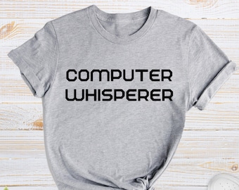 May include: A gray t-shirt with the text "COMPUTER WHISPERER" printed in black.