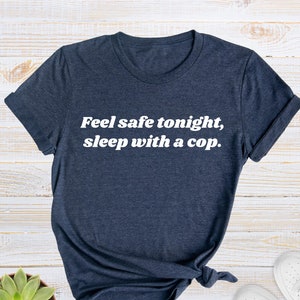 May include: A dark blue t-shirt with the text "Feel safe tonight, sleep with a cop." printed in white.
