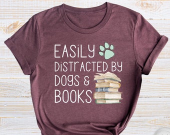 May include: A maroon t-shirt with the text "EASILY DISTRACTED BY DOGS & BOOKS" and a green paw print. A stack of books is pictured next to the text.