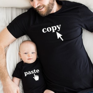 May include: A father and son wearing matching black t-shirts. The father's shirt says "copy" with a computer mouse cursor. The son's shirt says "paste" with a computer mouse cursor.