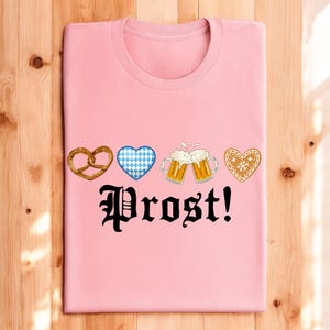 A pink t-shirt with the text "Prost!" printed on it, along with four heart-shaped icons representing pretzels, beer mugs, and gingerbread cookies.
