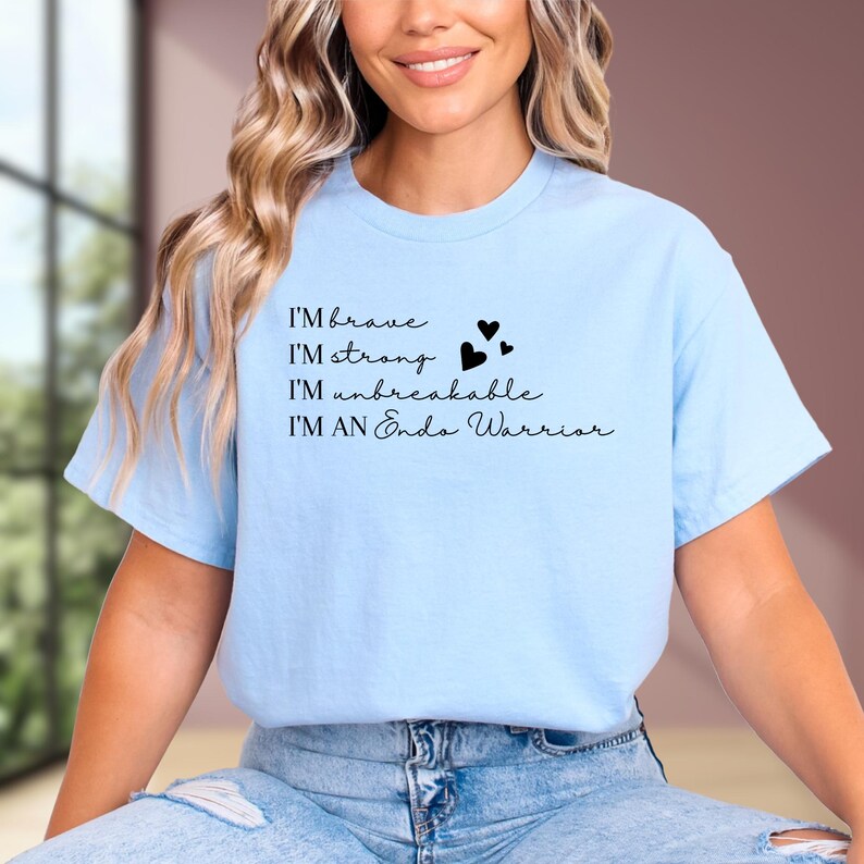 May include: A light blue t-shirt with the phrases "I'M brave, I'M strong, I'M unbreakable, I'M AN Endo Warrior" in black script. Three black hearts are printed next to the phrase "I'M strong". The shirt is made of a soft material.