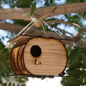 May include: A wooden birdhouse with a rounded shape and a small entrance hole. The birdhouse is hanging from a tree branch with a white string.