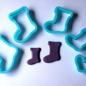 May include: Five blue plastic cookie cutters shaped like Christmas stockings, and two purple fondant Christmas stockings.